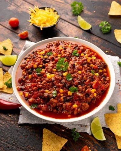 Bowl of mixed bean chili, topped with fresh coriander, surrounded by tortilla chips