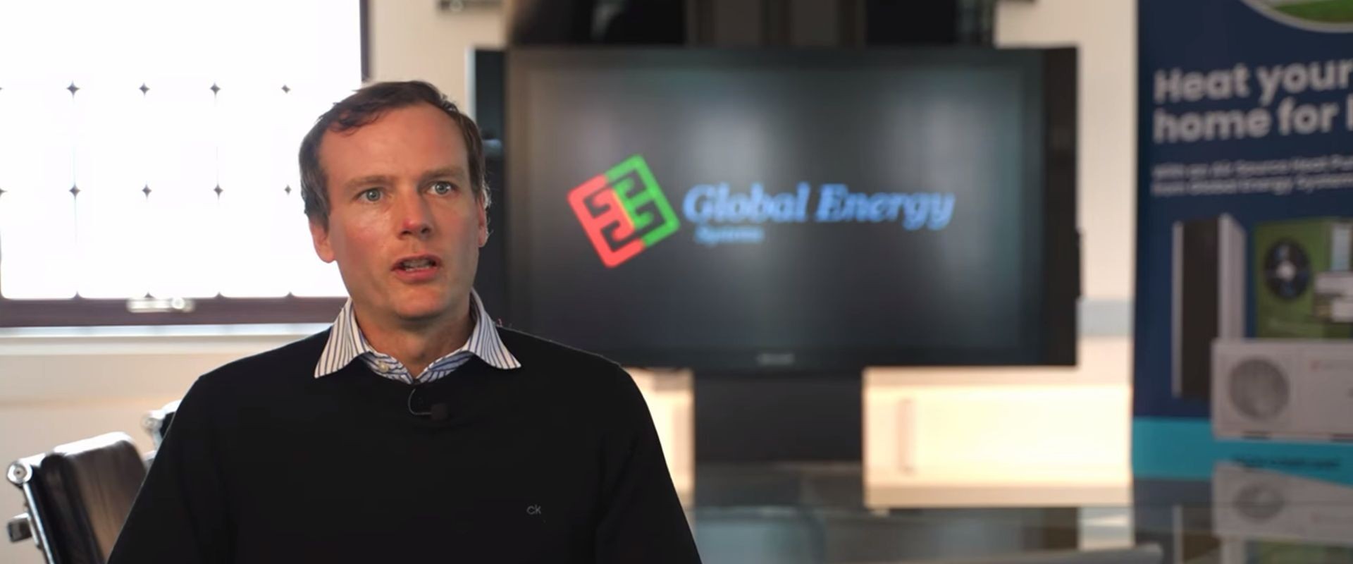 Global Energy Systems employee sat in front of the logo talking to camera